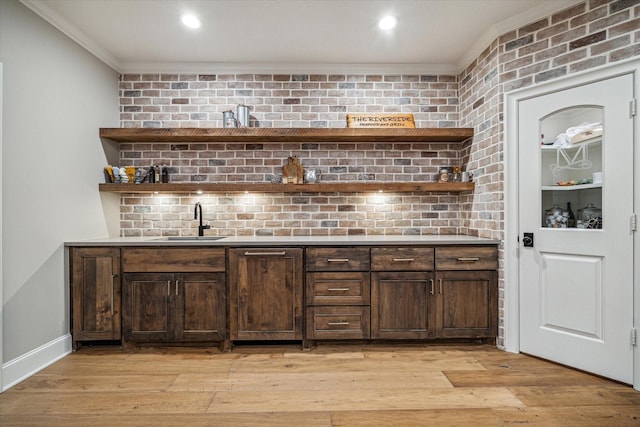 bar with light wood finished floors, brick wall, crown molding, baseboards, and a sink