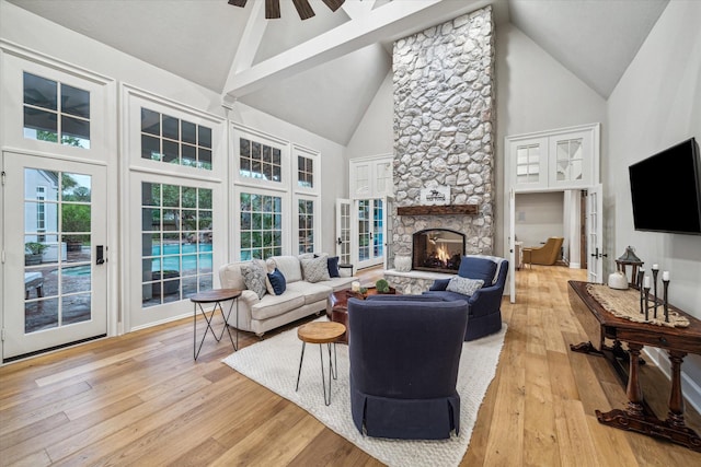 living area with high vaulted ceiling, a ceiling fan, french doors, light wood-style floors, and a fireplace