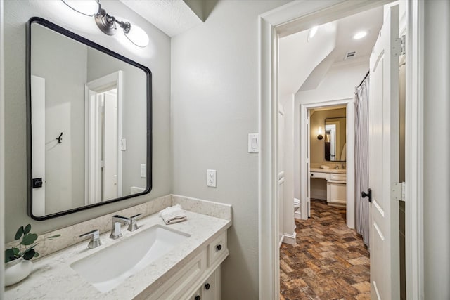 bathroom featuring vanity, toilet, and brick floor