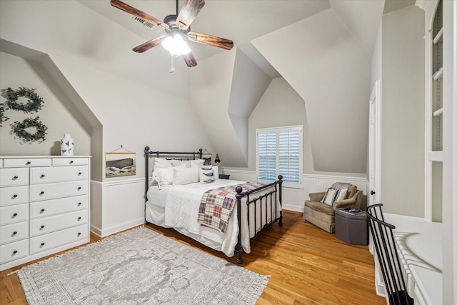 bedroom with light wood-type flooring, a wainscoted wall, lofted ceiling, and a ceiling fan