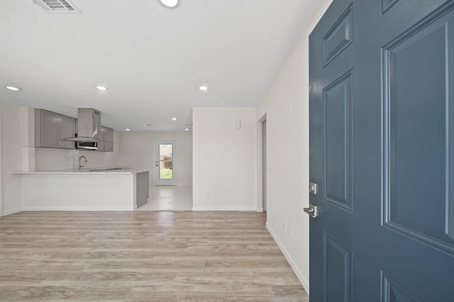 unfurnished living room with visible vents, light wood-style flooring, a sink, recessed lighting, and baseboards