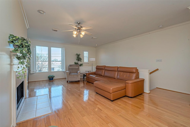 living area featuring baseboards, a fireplace, ceiling fan, ornamental molding, and light wood-style floors