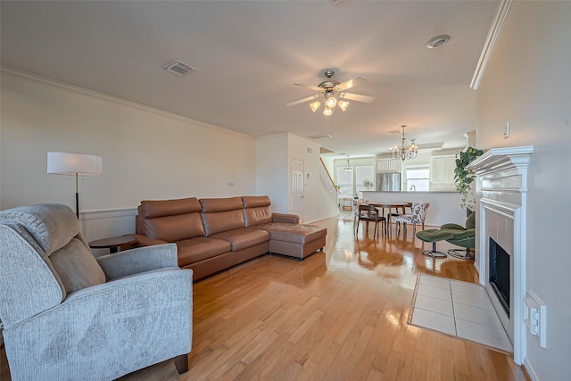 living room featuring visible vents, a fireplace with flush hearth, ornamental molding, and light wood finished floors