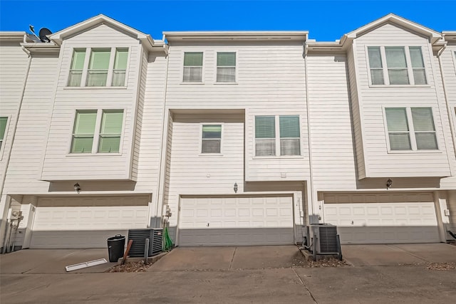 rear view of property featuring driveway, an attached garage, and central AC