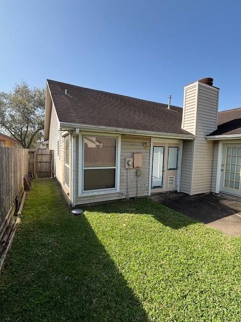 back of property featuring a lawn, a chimney, a fenced backyard, and a shingled roof