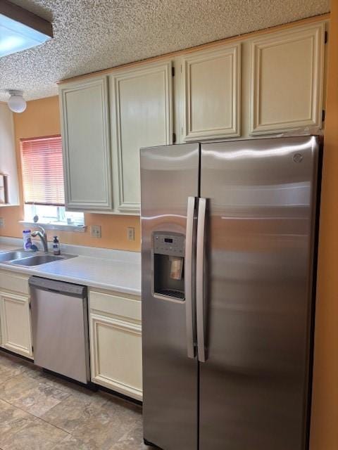 kitchen featuring light countertops, cream cabinets, stainless steel appliances, a textured ceiling, and a sink