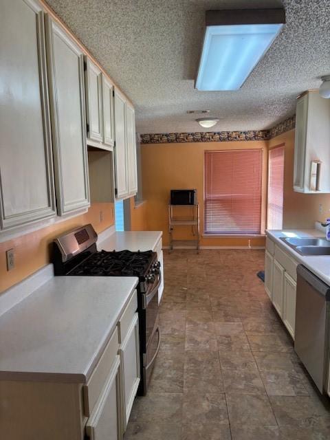 kitchen featuring a sink, stainless steel appliances, light countertops, white cabinets, and a textured ceiling