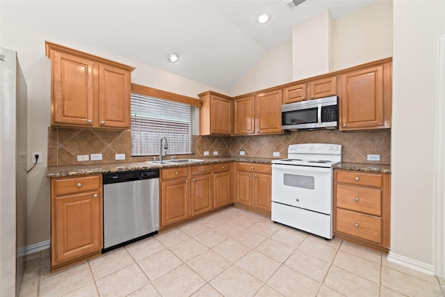 kitchen with a sink, lofted ceiling, dark stone counters, and stainless steel appliances