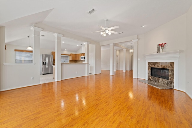 unfurnished living room featuring visible vents, a ceiling fan, a premium fireplace, decorative columns, and lofted ceiling