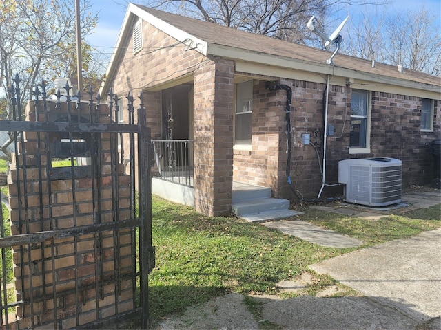 view of side of home with cooling unit, brick siding, and a gate