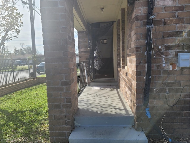 view of exterior entry featuring fence and brick siding