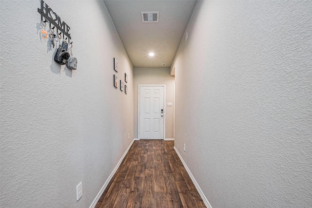 hallway featuring visible vents, baseboards, dark wood finished floors, and a textured wall