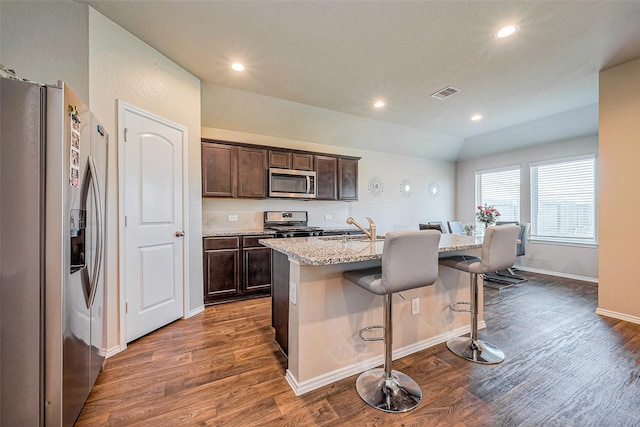 kitchen with visible vents, a kitchen island with sink, a sink, stainless steel appliances, and dark wood-style flooring