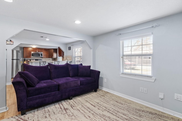 living area featuring recessed lighting, baseboards, light wood-style floors, and a textured ceiling