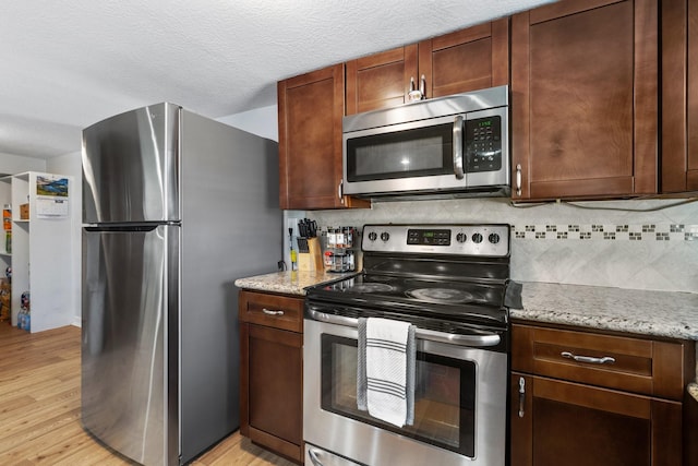 kitchen with light stone counters, backsplash, light wood-style floors, and appliances with stainless steel finishes