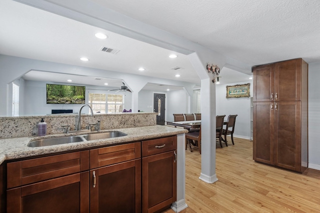 kitchen featuring open floor plan, light stone counters, light wood-style flooring, recessed lighting, and a sink