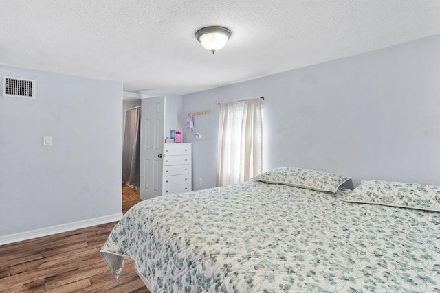 bedroom featuring a textured ceiling, wood finished floors, visible vents, and baseboards