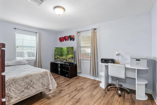 bedroom featuring visible vents, a textured ceiling, baseboards, and wood finished floors