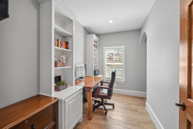 home office featuring arched walkways, baseboards, and light wood-style floors