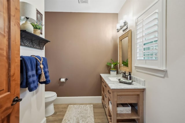 half bath with baseboards, toilet, wood finished floors, and vanity