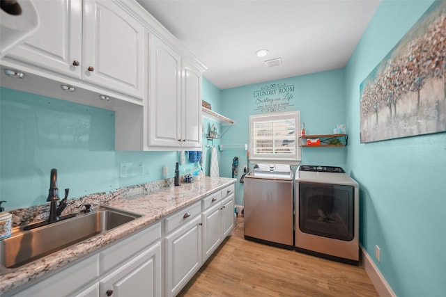 laundry room featuring baseboards, light wood-type flooring, separate washer and dryer, cabinet space, and a sink