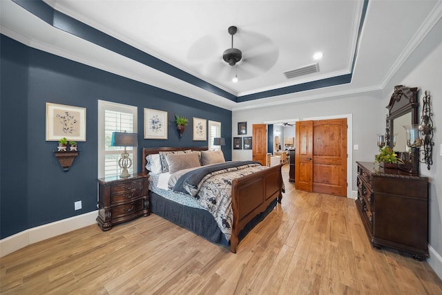 bedroom featuring baseboards, visible vents, a tray ceiling, light wood-style flooring, and ornamental molding