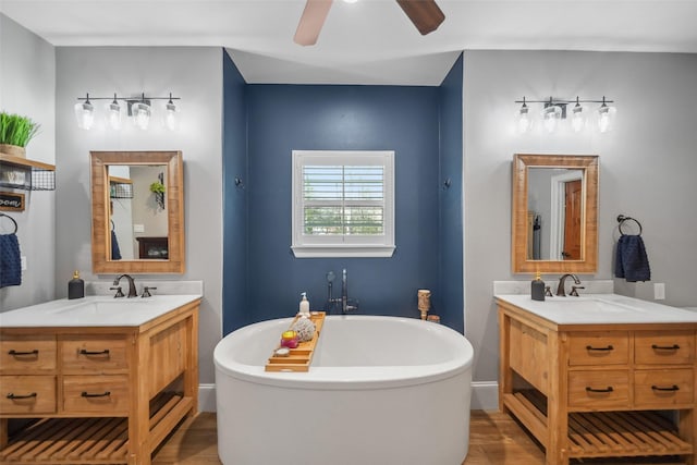 full bath with a sink, a freestanding bath, two vanities, and wood finished floors