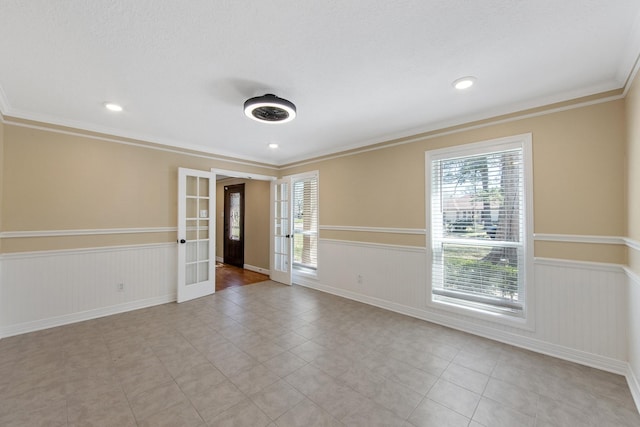 spare room featuring crown molding, french doors, a wainscoted wall, and a wealth of natural light