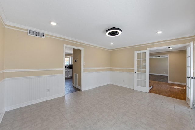 unfurnished room with a wainscoted wall, crown molding, french doors, and visible vents