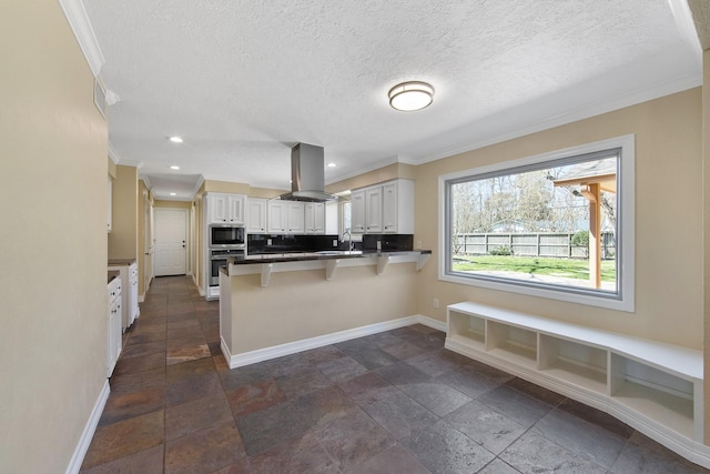 kitchen with island exhaust hood, a sink, a peninsula, appliances with stainless steel finishes, and baseboards