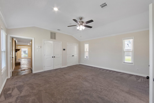 unfurnished bedroom with lofted ceiling, visible vents, multiple closets, and dark carpet