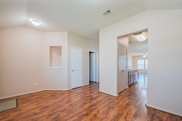 spare room featuring dark wood finished floors, visible vents, baseboards, and lofted ceiling