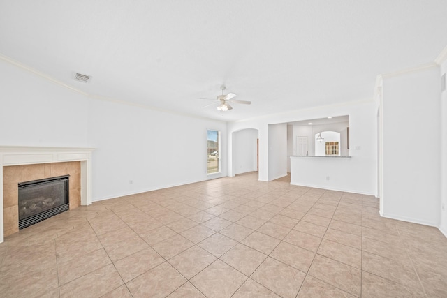 unfurnished living room featuring baseboards, arched walkways, ornamental molding, ceiling fan, and a tiled fireplace