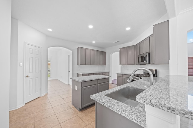 kitchen with a sink, stainless steel appliances, arched walkways, and light stone countertops