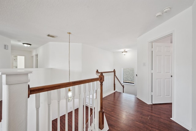 hallway featuring visible vents, an upstairs landing, a textured ceiling, wood finished floors, and baseboards