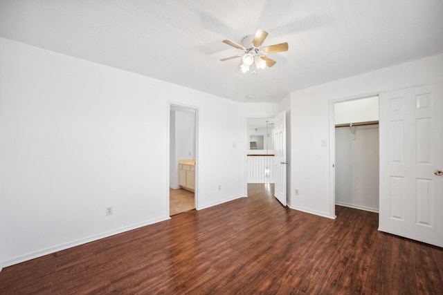 unfurnished bedroom featuring a walk in closet, dark wood-type flooring, baseboards, and a closet