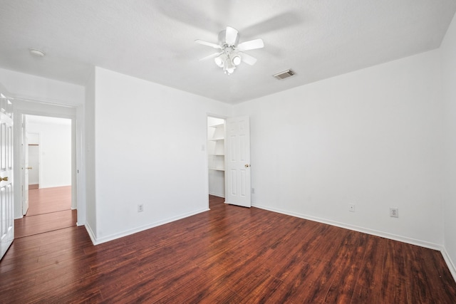 unfurnished bedroom featuring a spacious closet, visible vents, ceiling fan, baseboards, and wood finished floors