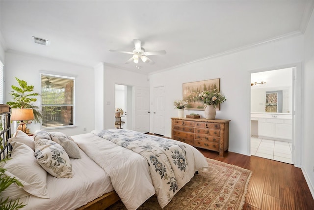 bedroom with visible vents, crown molding, ceiling fan, ensuite bathroom, and wood finished floors