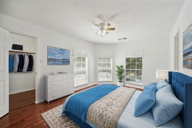 bedroom with a spacious closet, visible vents, baseboards, dark wood-style floors, and a ceiling fan