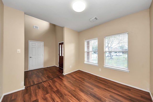 spare room featuring visible vents, baseboards, and dark wood-style flooring