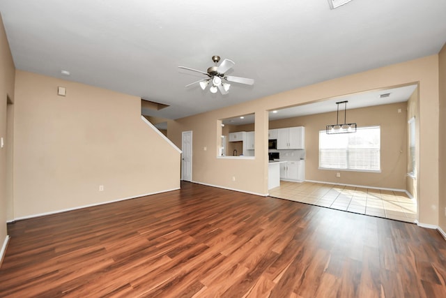 unfurnished living room featuring ceiling fan with notable chandelier, stairs, wood finished floors, and baseboards