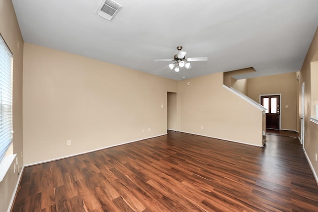 empty room featuring stairway, dark wood-style floors, visible vents, and ceiling fan