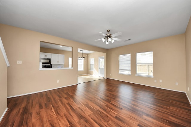 unfurnished living room with a ceiling fan, visible vents, dark wood-style floors, and baseboards