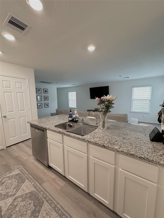 kitchen featuring visible vents, light wood-style flooring, stainless steel dishwasher, white cabinets, and a sink