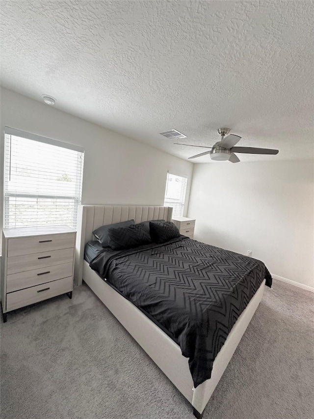 bedroom with visible vents, light colored carpet, ceiling fan, and a textured ceiling