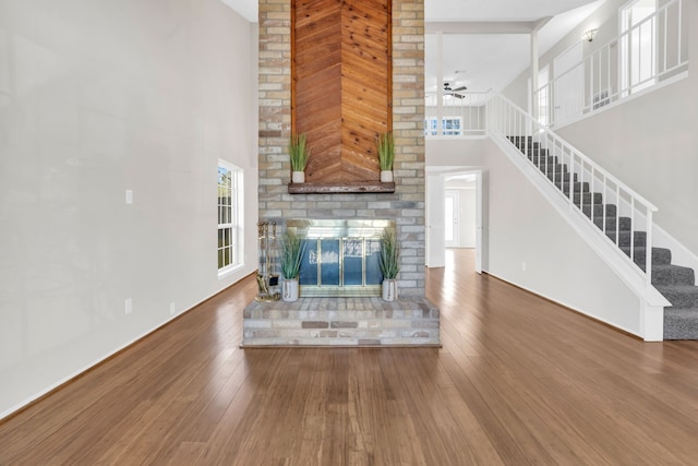 unfurnished living room with a high ceiling, stairs, ceiling fan, and wood-type flooring