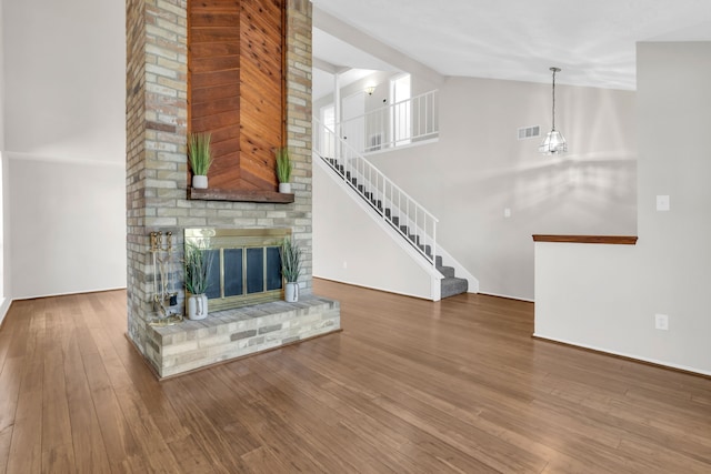 unfurnished living room featuring visible vents, high vaulted ceiling, wood finished floors, a fireplace, and stairs