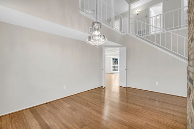 unfurnished living room featuring visible vents, a chandelier, stairway, hardwood / wood-style floors, and a high ceiling