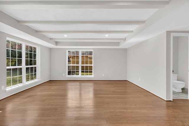 empty room with beamed ceiling, plenty of natural light, and wood finished floors