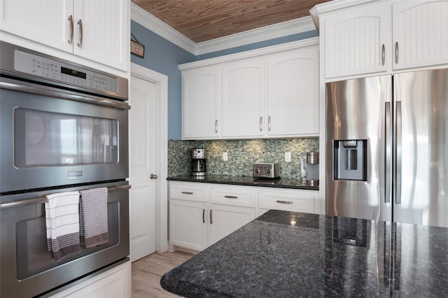 kitchen featuring dark stone countertops, backsplash, white cabinetry, stainless steel appliances, and crown molding